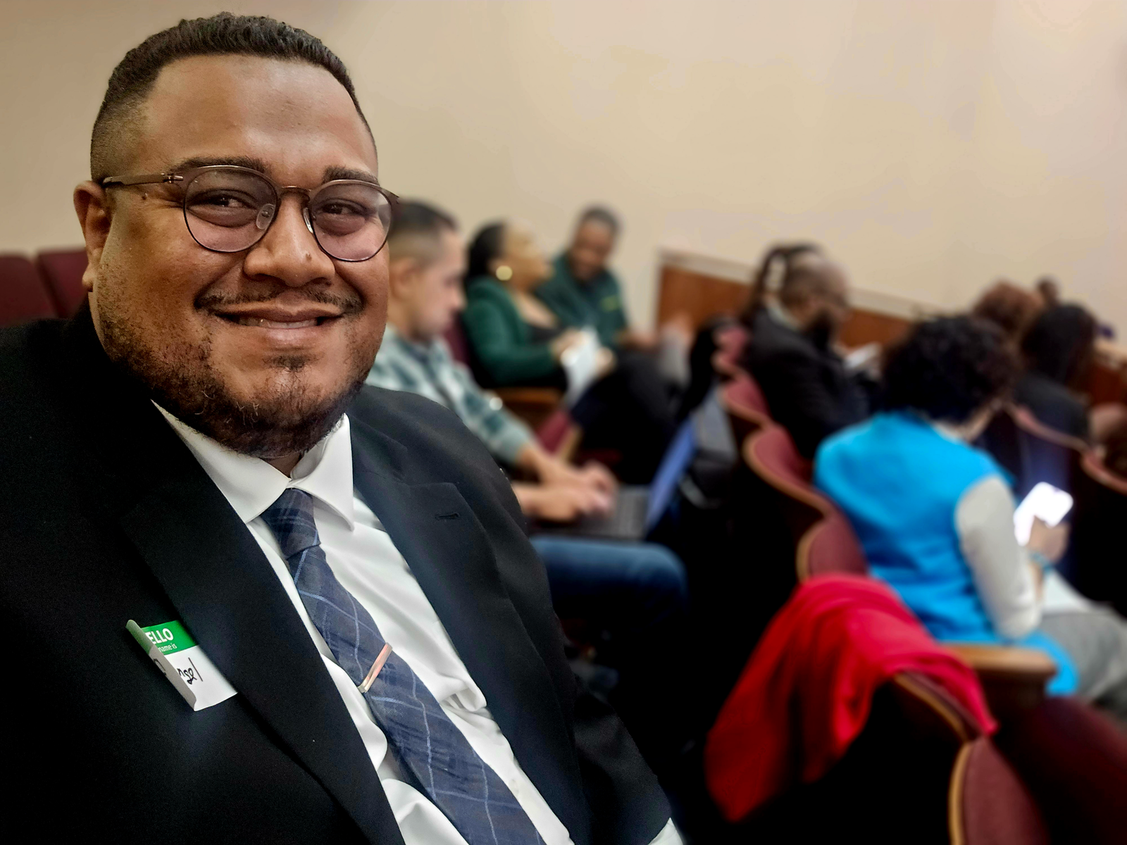 Dr. Angel L. Velez seated among community members at a public hearing in Chicago