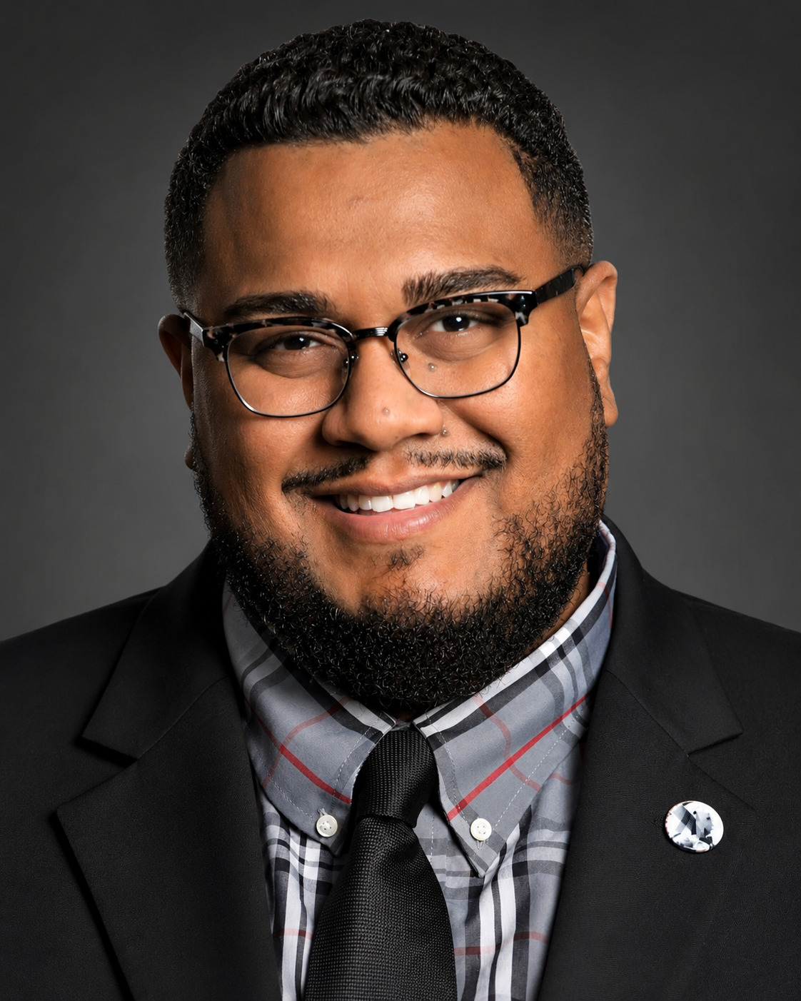 Press headshot of Dr. Angel L. Velez, studio portrait in a black suit