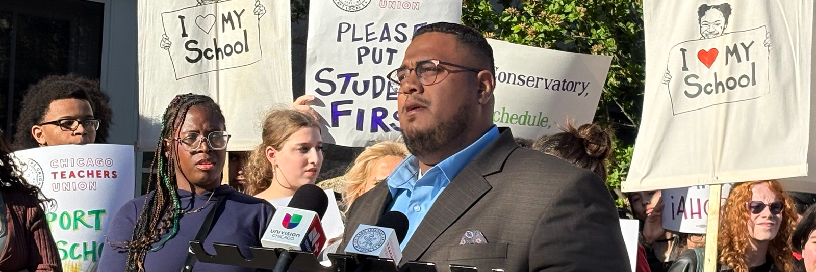 Dr. Angel L. Velez speaking at a press conference surrounded by students and educators holding I Love My School signs